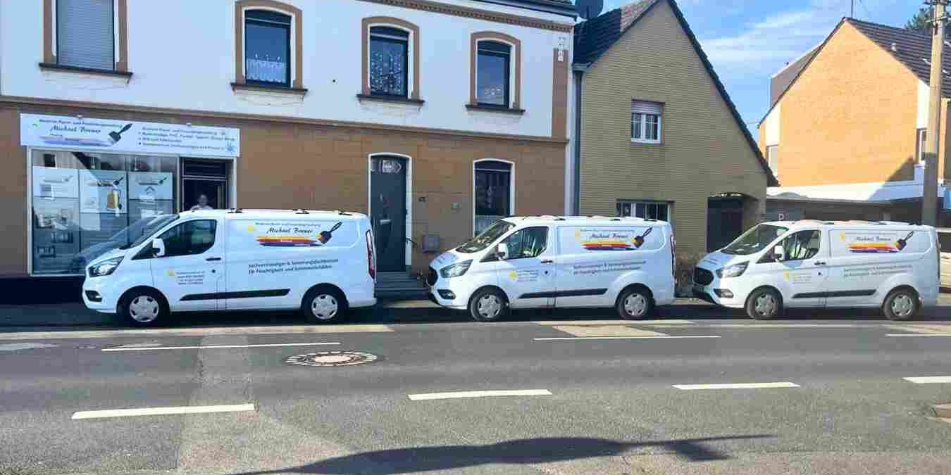 Drei weiße Lieferwagen von Michael Breuer Raumgestaltung parken vor dem Büro in Rondorf.