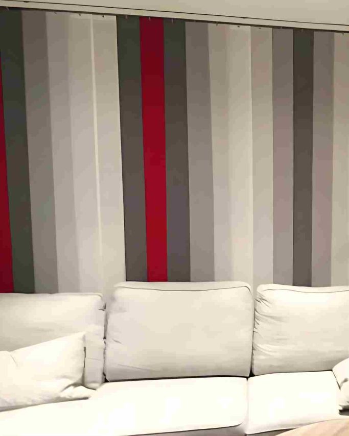 Gestreifte Wand in Grau mit roten und grauen Streifen, davor ein helles Sofa.
