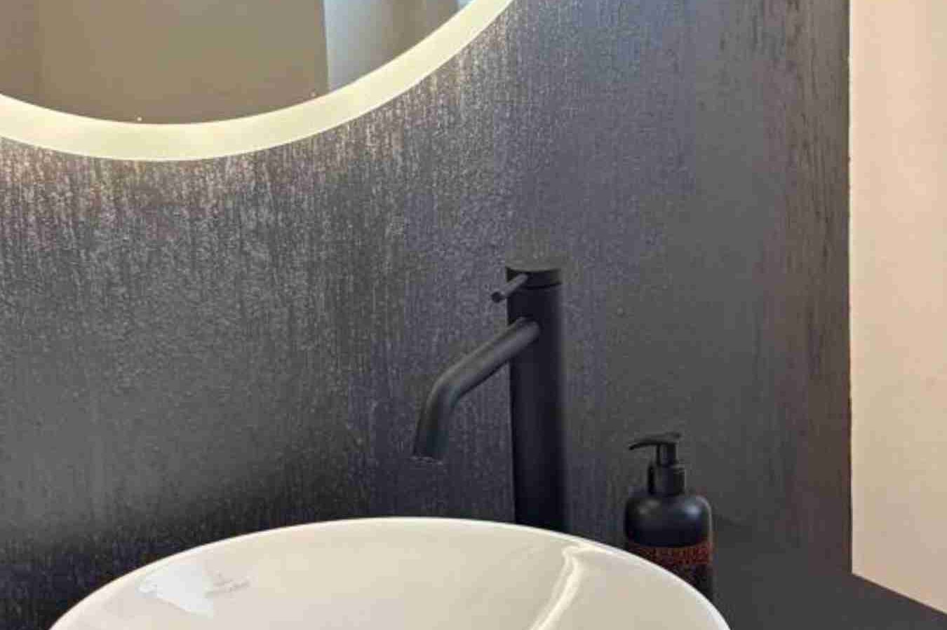 Moderne Wandgestaltung in Kölner Bad. Moderne Badezimmeransicht mit einem runden Spiegel und einem eleganten Waschbecken. Die Wände sind moderner Wandtechnik in Grau gestrichen.
