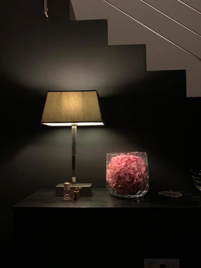 Tischlampe neben einer gläsernen Vase mit pinken Blumen auf schwarzem Hintergrund.