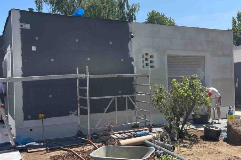 Bauarbeiten an einem Haus, teilweise verputzte Wand, Arbeiter und Materialien sichtbar. Die Dämmungen sind teils schon angebracht.