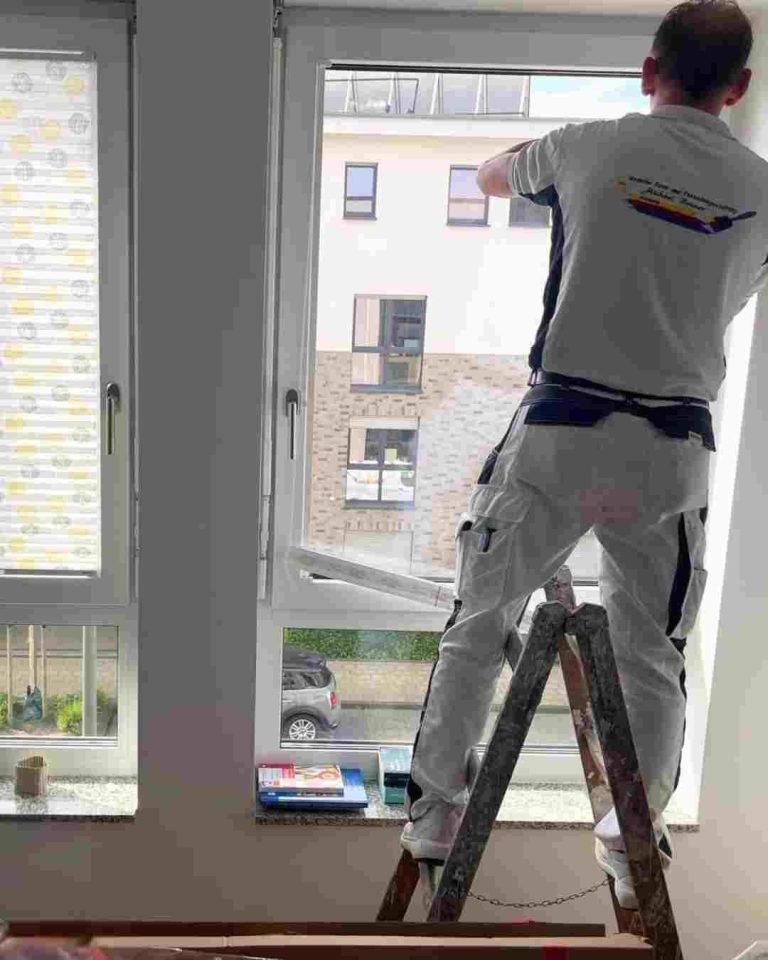 Ein Mitarbeiter von Raumgestaltung Breuer steht auf einer Leiter und bringt Sichtschutz in einem Wohnhaus an. 