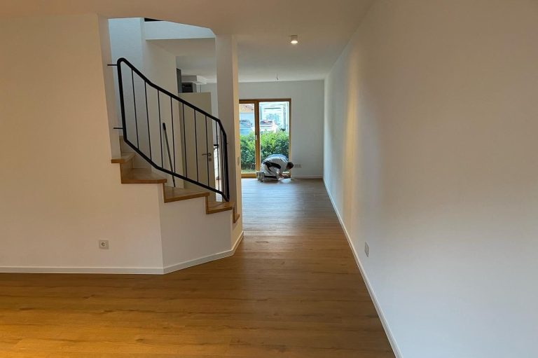 Neuer Pakettboden Köln Heller Flur mit Holzfußboden und Treppe, Blick auf einen Gartenbereich. Neu verlegter Paketboden