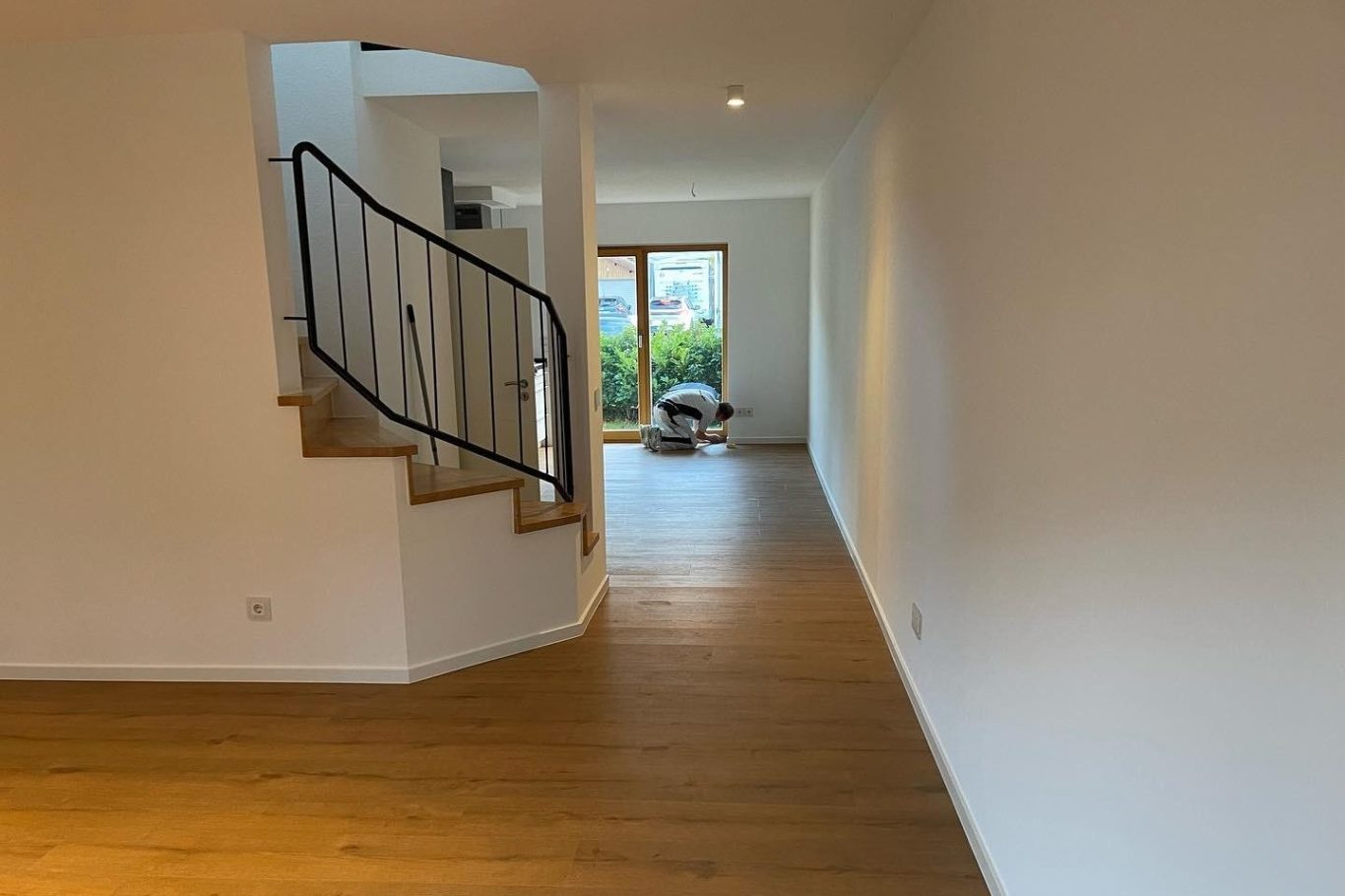 Parkettboden in Köln Heller Flur mit Holzfußboden und Treppe, durch die Tür ist ein Garten sichtbar. Neuer Parkettboden verlegt in einem Haus in Köln