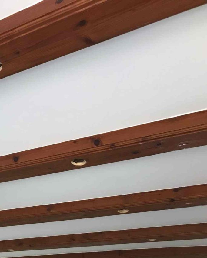 Holzbalken an einer weißen Decke mit sichtbaren Nägeln und Maserungen.