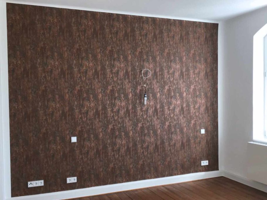 Braune Tapete mit strukturierter Oberfläche an einer leeren Wand, weißen Steckdosen.