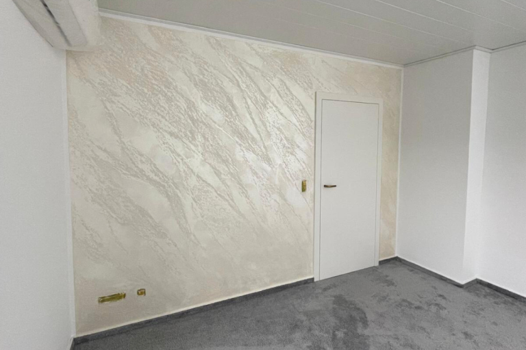 Putztechnik auf Wand Raum mit strukturiertem, hellem Wandbelag und geschlossener Tür auf einer grauen Bodenfläche.