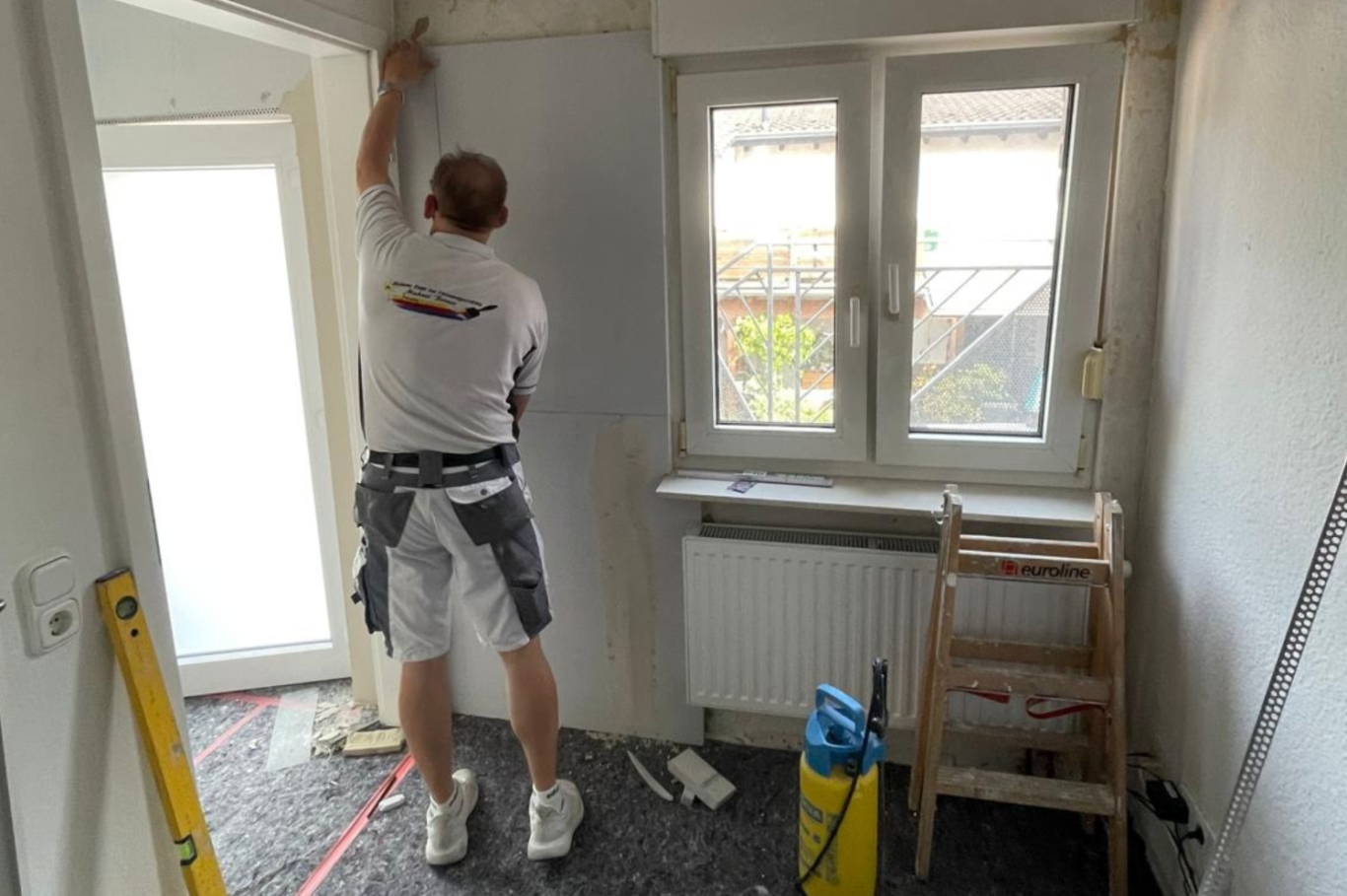 Handwerker bei der Schimmelsanierung Handwerker renoviert einen Raum, während er Schimmelschutzplatten an die Wand anbringt.