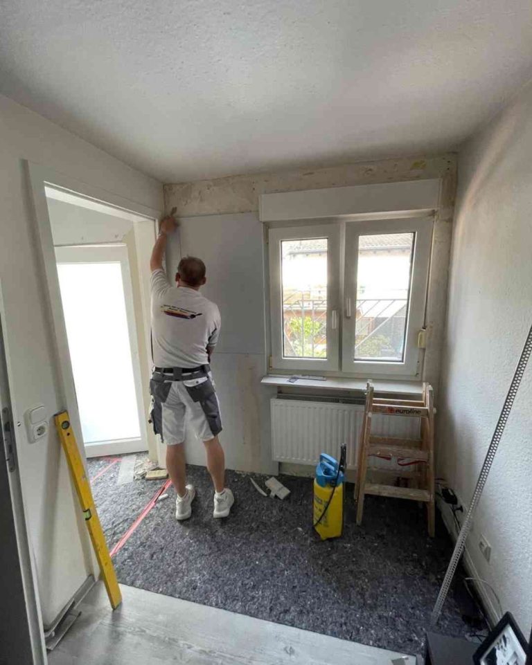 Schimmelsanierung Handwerker von Raumgestaltung Breuer bringt Platten gegen Schimmel an der Wand in einem Raum an.