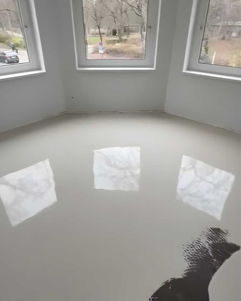 Boden mit glänzender, reflektierender Oberfläche und Fenstern im Hintergrund. Ausgleichsmasse zur Bodenverlegung wird verteilt.