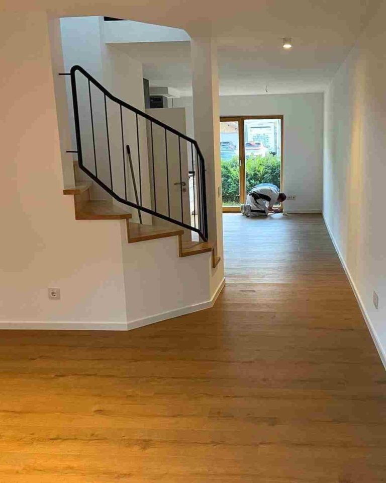 Heller Wohnraum mit Holzfußboden, Treppe und Zugang zu einem Balkon. Parkettboden wird verlegt von Raumgestaltung Breuer.