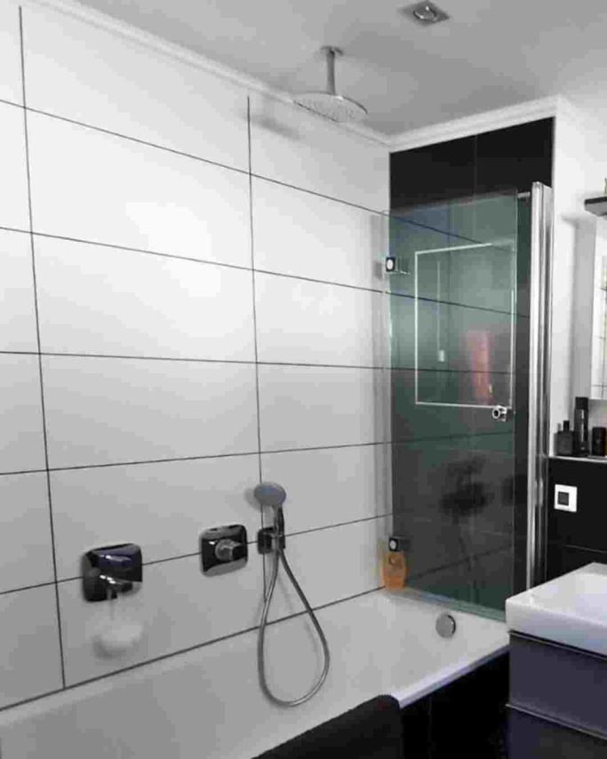 Modernes Badezimmer mit Dusche, Glasabtrennung und weißen Fliesen.