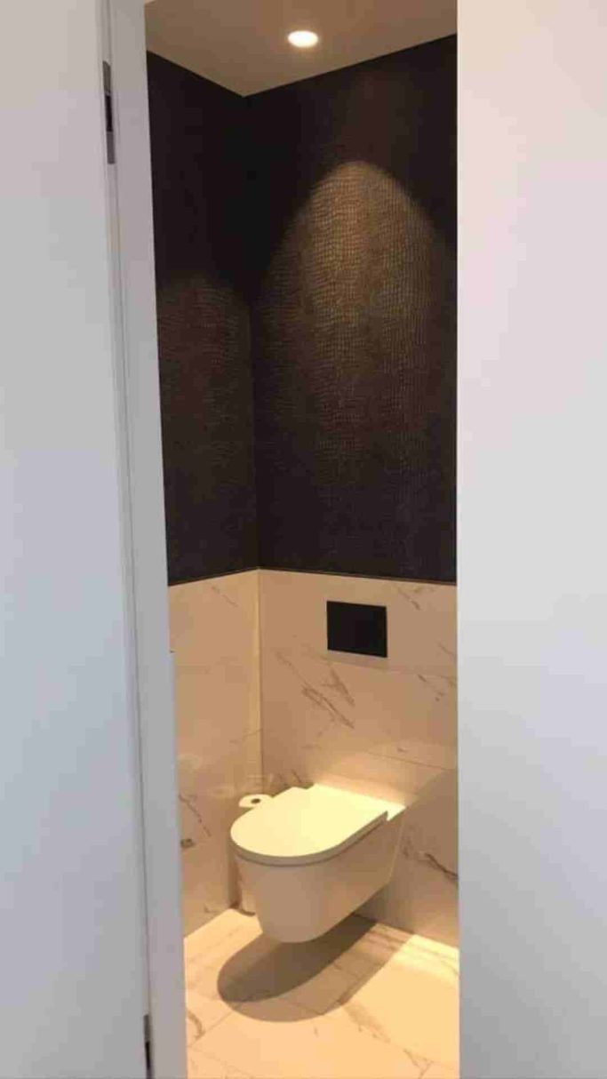 Modernes Badezimmer mit einer Wandtoilette vor einem dunklen Wanddesign.