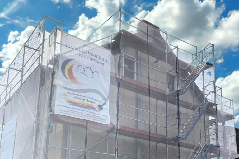 Einfamilienhaus mit Baugerüst und Banner, unter blauen Himmel und Wolken.
