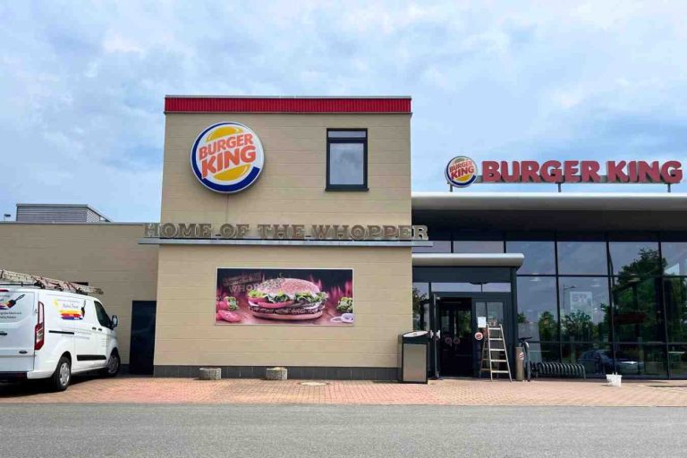 Burger King Restaurant mit Logo und Werbebanner für Burger. Davor ein Firmenwagen von Raumgestaltung Breuer. Neue Fassade erstellt.